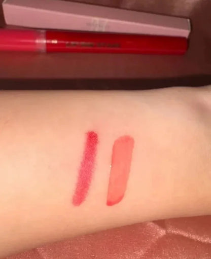Two lipstick swatches on a person's inner forearm, showing a textured red shade and a smooth coral-pink shade, with a red lip product tube and its box partially visible in the background.
