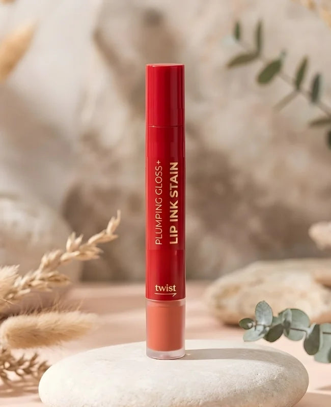 Red lip gloss tube labeled 'Plumping Gloss Lip Ink Stain' on a stone surface with natural background