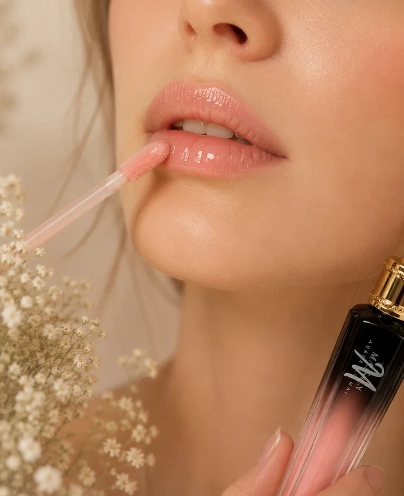Close-up of a woman applying a glossy pink lip product with a doe-foot applicator, holding a black-to-pink gradient tube with a gold cap.