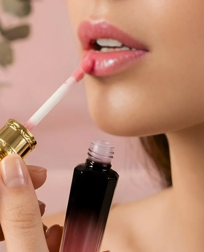 Person applying lip gloss with a brush on a pink background